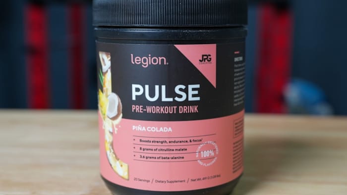 Black tub with a pink label with white writing that reads "PULSE PRE-WORKOUT DRINK" on a table